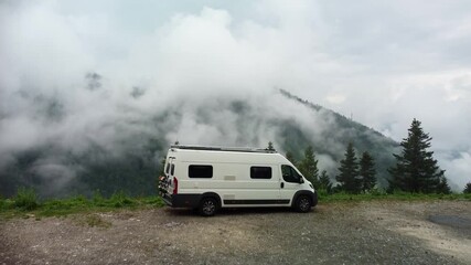 Wall Mural - Drone video of a camper van parked on the edge of a mountain with low lying clouds in the valley. Footage moves over the Motorhome to reveal the stunning views behind of the clouds in forest.