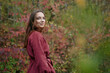 © SHOTPRIME STUDIO - A candid portrait of a young woman in a burgundy coat, standing among autumn foliage, conveying authenticity and sincere mood, quiet confidence, natural pose, subtle smile.