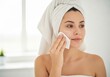© Ektarul - Young woman with a towel on her head cleaning her face with a cotton pad after a shower in a bright bathroom at home