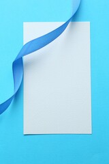Wall Mural - Beautiful ribbon and blank card on light blue background, flat lay