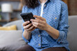© Liubomir - Woman sitting on a sofa at home, scrolling on a mobile phone, communicating online using modern technology, browsing internet pages or social media applications