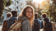 © Dirk - Group of young people with backpacks, smiling towards the camera in front of university building on campus. Woman is looking from behind her shoulder, carrying a canvas bag. University students.