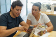 © Gener Vázquez - Dos colegas latinos discuten contenido en un smartphone y laptop, colaborando en un espacio de trabajo moderno.