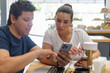 © Gener Vázquez - Pareja de negocios latina colaborando en un smartphone en una cafetería moderna.