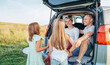 © Soloviova Liudmyla - Portrait of Happy young couple with little daughters sitting inside car trunk during auto trop. They are smiling, laughing and chatting. Family values, traveling concept.