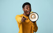 © Prostock-studio - It is your chance. Emotional young guy with megaphone making announcement on blue studio background, african american man saying something loud and pointing at camera, copy space
