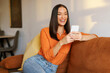 © Home-stock - Happy young woman relaxing on comfortable couch, holding smartphone, chatting in social networks, watching videos or using mobile applications