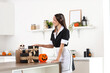 © Pixel-Shot - Young happy woman dressed as dead maid for Halloween with gift boxes, human skull and pumpkin on table in kitchen
