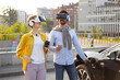 © sofiko14 - A couple wearing VR headsets while an electric vehicle charges in an urban setting.