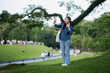 © Oil And Den - A young woman video calling outdoors in a park, smiling happily and enjoying a relaxing day.