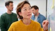 © Z A C - Asian woman in office setting, pointing at whiteboard during presentation.