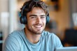 © Olya - Young man with headphones smiling while sitting indoors, enjoying music or audio content in a cozy environment