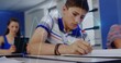 © vectorfusionart - Writing student in striped polo shirt focusing on notebook at school, with pen tablet desks chairs