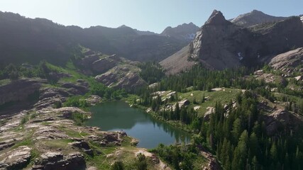 Wall Mural - Aerial drone trucking right shot of Lake Blanche in Big Cottonwood Canyon near Salt Lake City, Utah, on a bright green summer morning with rocky peaks, lush foliage, and Sundial Peak towering above