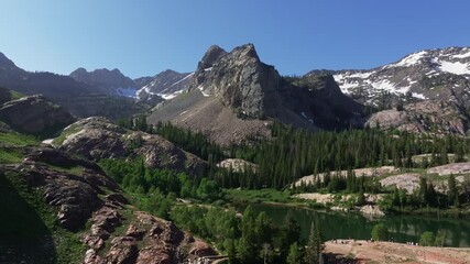 Wall Mural - Aerial drone dolly in wide shot of Lake Blanche in Big Cottonwood Canyon near Salt Lake City, Utah, on a bright green summer morning with rocky peaks, lush foliage and Sundial Peak towering above