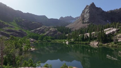 Wall Mural - Aerial drone dolly out shot of Lake Blanche in Big Cottonwood Canyon near Salt Lake City, Utah, on a bright green summer morning with rocky peaks, lush foliage, and Sundial Peak towering above