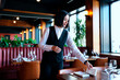 © Seventyfour - Young adult Caucasian woman arranging table settings in restaurant, placing napkin and adjusting glassware, working as waitress with short dark hair, focused on preparing dining area
