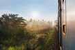 © Travel 'n' Lifestyle - View of golden sunlight piercing through the misty landscape as seen from a train window, casting long shadows across the tracks, Kandy, Central Province, Sri Lanka.