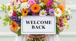 © ALAUDDIN - Woman holding a bouquet of colorful flowers with a welcome back sign
