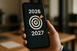 © ParinApril - Modern smartphone in hand displaying targets and goals for 2026 and 2027 in a professional setting