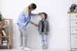 © New Africa - Mother measuring height of her little son near white wall indoors