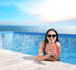 © New Africa - Woman drinking cocktail in swimming pool with infinity view on ocean