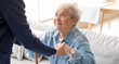 © Pixel-Shot - Young caregiver helping senior woman with stick to stand up at home