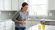 © Meow Creations - Woman in modern kitchen experiencing intense stomach pain, clutching her abdomen with a pained expression