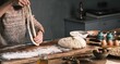 © Damian - A person stretches dough on a floured wooden board, preparing to bake. Eggs, flour, nuts, and other items sit nearby, ready for use in the baking process on a rustic table