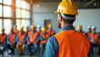 © Viktor - Construction worker in yellow helmet, orange vest teaches safety briefing to group of men. Foreman leads workshop for building crew at job site. Engineers, builders learn important protection rules