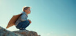 © Viktor - Young boy with homemade cardboard wings squats on rock, looking up into vast blue sky. Dreams of flying, imagining future full of success, adventure. Child visualizes becoming pilot, leader,