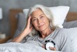 © homeganko - Senior Woman Relaxing in Bed With a Morning Alarm Clock on a Peaceful Day