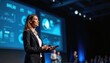 © Viktor - Businesswoman gives speech at conference stage. Female presenter with presentation remote controls data screen behind. Public speaking at business event. Audience watching. Professional woman in suit