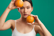 © SHOTPRIME STUDIO - Asian woman holds oranges against a green backdrop, creating a fresh, vibrant portrait. She looks toward the camera with a calm, engaging expression.