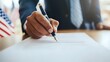 © Yuliia - African American businessman signing legal document at office desk with American flag in background, professional corporate setting for business contracts.