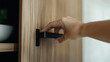 © photo for everything - A hand opening a wood-paneled cabinet with a sleek, modern black handle. Soft light highlights the textured wood and the smooth curve of the hand, creating a clean, inviting image.