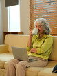 © Stella 16 - Happy Asian 60s retired woman enjoys social media on laptop while relaxing in living room.