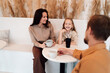 © BullRun - Daughter laughs with mother during casual coffee time, both enjoying relaxed family interaction while father listens in, symbolizing balance and joy in parenting.