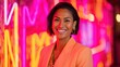 © mila103 - A woman in a bright orange jacket is smiling at the camera. The neon lights in the background create a vibrant and energetic atmosphere
