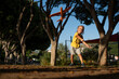 © sutulastock - Energetic young blond boy throwing an orange toy airplane in a sunlit park, captured mid-motion with determination on his face and trees framing the scene in warm afternoon light