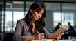 © satrio - A professional Asian businesswoman writing notes in a journal at her desk in a modern office.