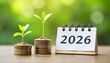 © Rama - Young green plants sprouting from stacks of coins beside a 2026 calendar, symbolizing growth, savings, and financial planning for the new year