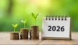© Rama - Young green plants sprouting from stacks of coins beside a 2026 calendar, symbolizing growth, savings, and financial planning for the new year