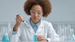 © 69 - Young Woman in Laboratory Conducting Experiment with Pipette and Blue Liquid Wearing Glasses in White Lab Coat, Focused Science Research Setting