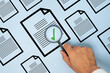 © izzuan - Hand holding a magnifying glass over a document with a green check mark. Document verification, quality control, audit, approval, compliance, and inspection concept.
