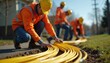 © Maryna - Team installs yellow fiber optic cables in suburban neighborhood. Workers in hard hats and safety vests lay conduit for new telecom infrastructure. Progress in telecommunications connection.