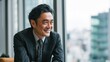 © Babb - A businessman smiles while sitting at a table in a contemporary office. The large windows reveal a vibrant city skyline suggesting a productive and positive atmosphere.