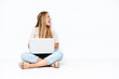 © luismolinero - Young woman with laptop sitting on the floor isolated on white background laughing in lateral position