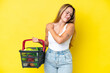 © luismolinero - Young caucasian woman holding a shopping basket full of food isolated on yellow background suffering from pain in shoulder for having made an effort