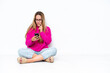 © luismolinero - Young caucasian woman sitting on the floor isolated on white background thinking and sending a message